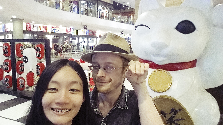 Ren and Ottie posing with a Maneki Neko fortune cat statue in Terminal 21 in Bangkok, Thailand.