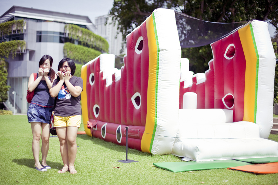 Photo of Ade and Puey posing in front of an inflatable plastic mockup of a watermelon see-saw at the Masak Masak exhibit at the National Museum of Singapore.