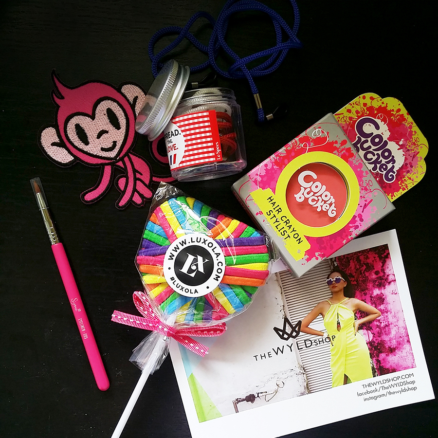 Flatlay beauty goodies: LeSpecs glasses holder, Color Bucket pink hair chalk, Luxola.com colourful hair ties in lollipop, The WYLD Shop postcard.