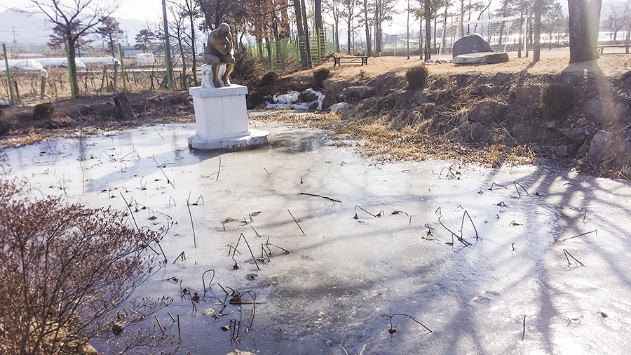 Pond frozen over with a Thinker statue in the middle in the school in the mountain, Sangju, South Korea.