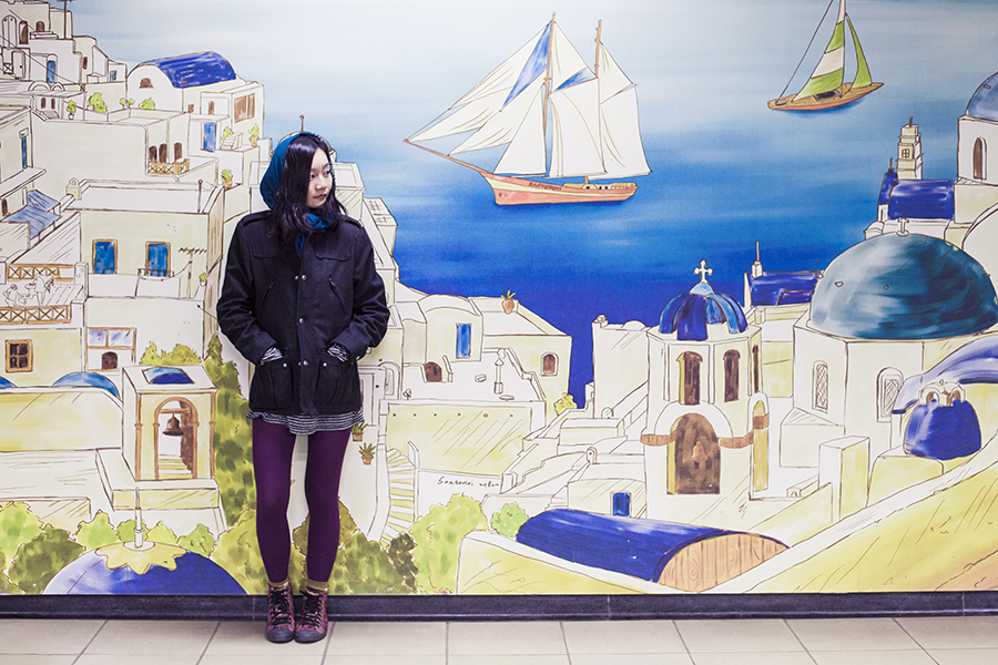 Outfit in front of a mural of Santorini, Greece on Seoul subway station, South Korea: H&M grey men's jacket, Marshalls gold studded shawl, Zara striped dress, Hue ribbed tights, Alexander McQueen x Puma red sneakers.
