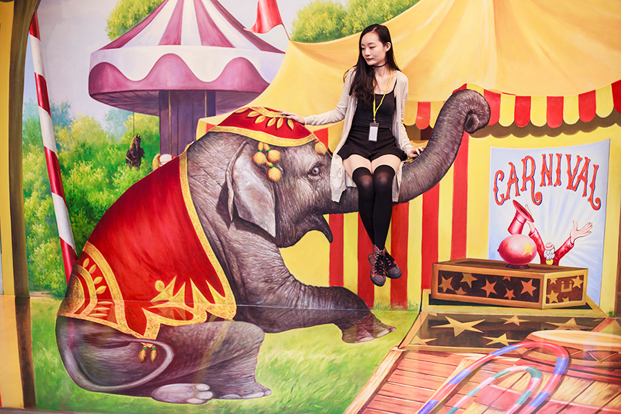 Sitting on a circus elephant's trunk at a trompe-l'œil at the Trick Eye Museum Renewal Event in Singapore, Resorts World Sentosa.
