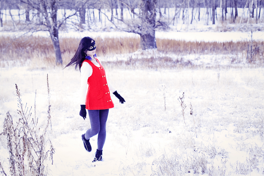 Self-portraiture photography in the snow- Feather masked red vest. Outfit details: gifted wool cape, thrifted red vest, Uniqlo cashmere sweater, River Island panda scarf, Forever21 knit tights, H&M blue feather hoop earrings, Fila boots.